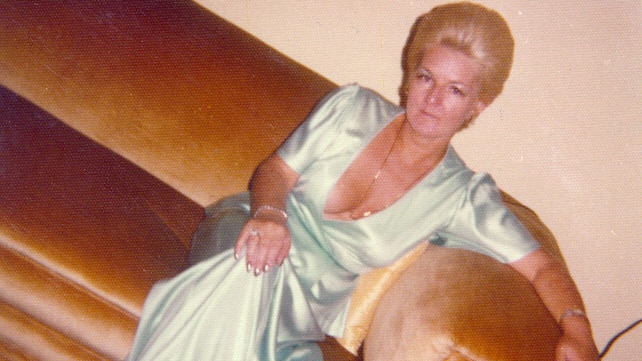 A vintage photograph of a woman in a long green dress sitting on a velour couch