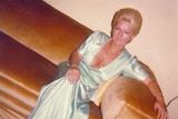 A vintage photograph of a woman in a long green dress sitting on a velour couch