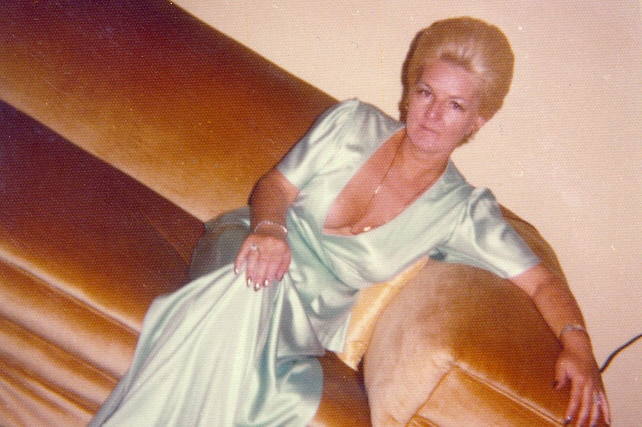 A vintage photograph of a woman in a long green dress sitting on a velour couch