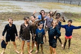 A group of children stand in a rainy field covered in mud.