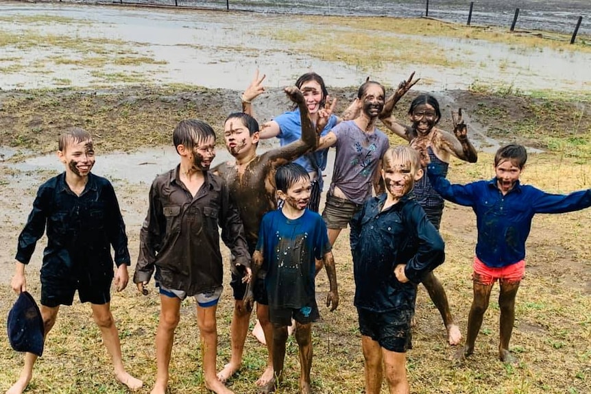 A group of children stand in a rainy field covered in mud.