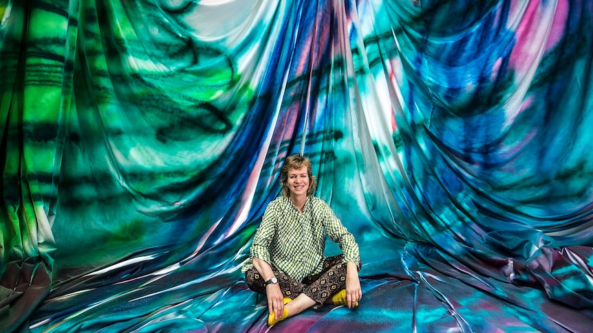 Artist Katharina Grosse sits cross-legged within her brightly coloured installation made from spray-painted fabric.
