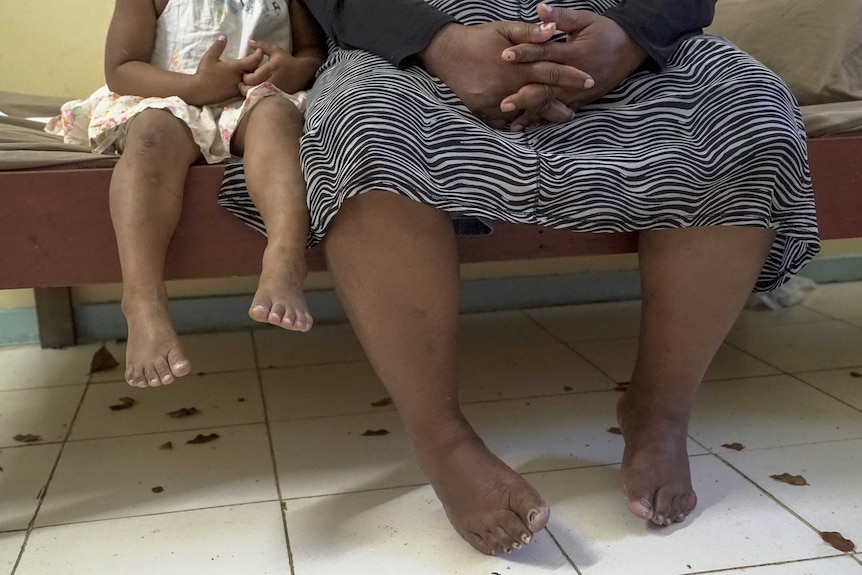 A woman sitting on a bed next to a small girl with her feet dangling over the side