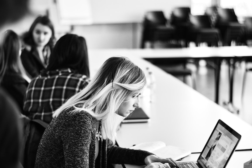 Black and white image of female high school student working on laptop in class