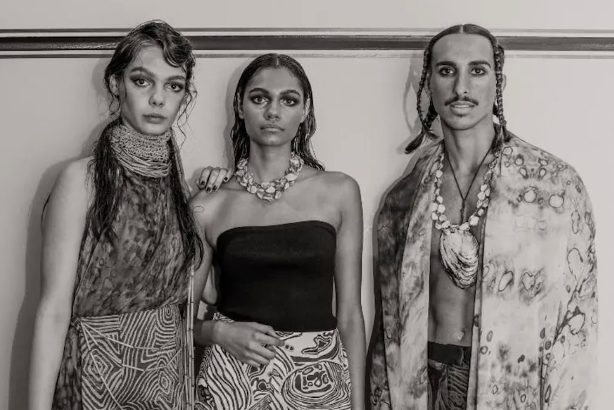 Three models pose in various pieces of fashion, in a black-and-white photo.