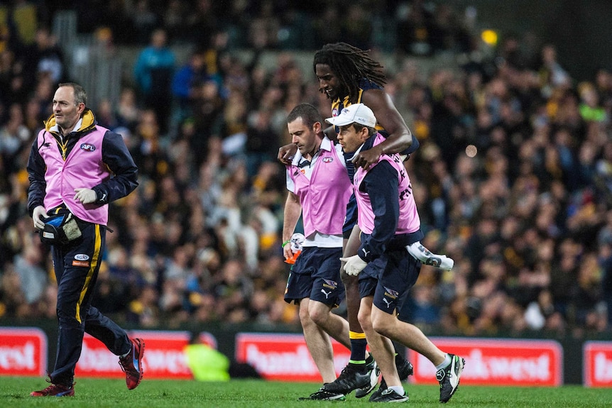 West Coast ruckman Nic Naitanui is helped from the field after injuring his knee against Hawthorn.