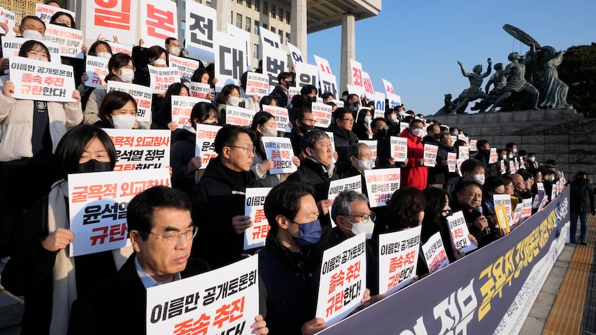 Rows of people stand on stairs each holding a sign with Korean writing on it. 