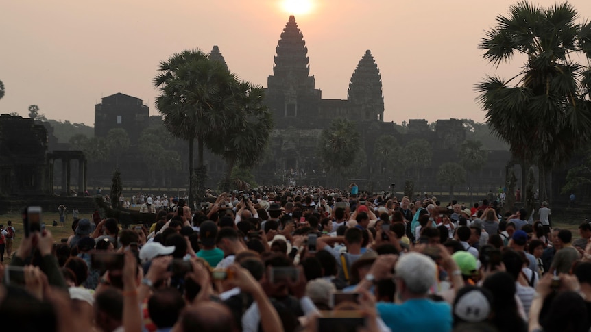 Hundreds of people line up in front of a temple as the sun rises.