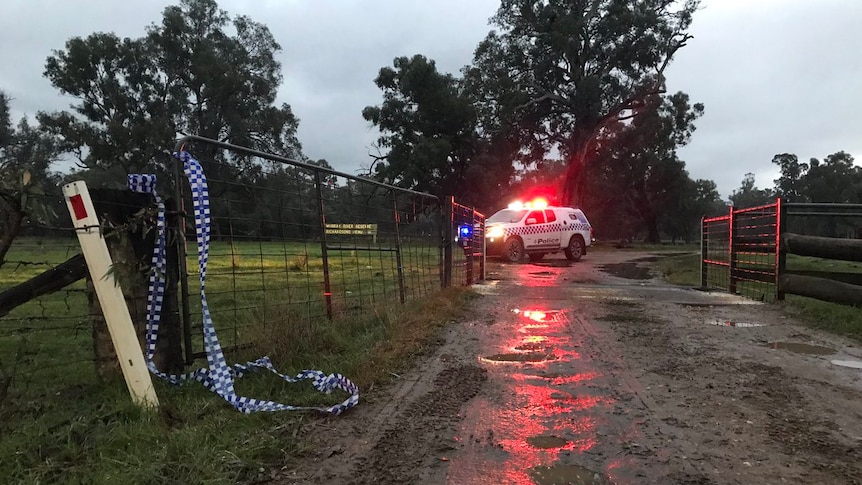 A police car with its lights on is parked in a muddy campground at dawn.