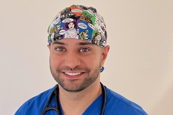 A man smiling in medical scrubs.