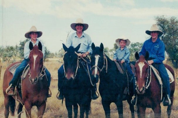 A woman and three children, all on horseback, dressed in blue work shirts and wide brim hats.