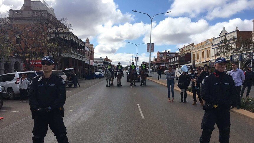 WA Police officers stand on Hannan Street, with members of the Mounted Police Unit in the background.