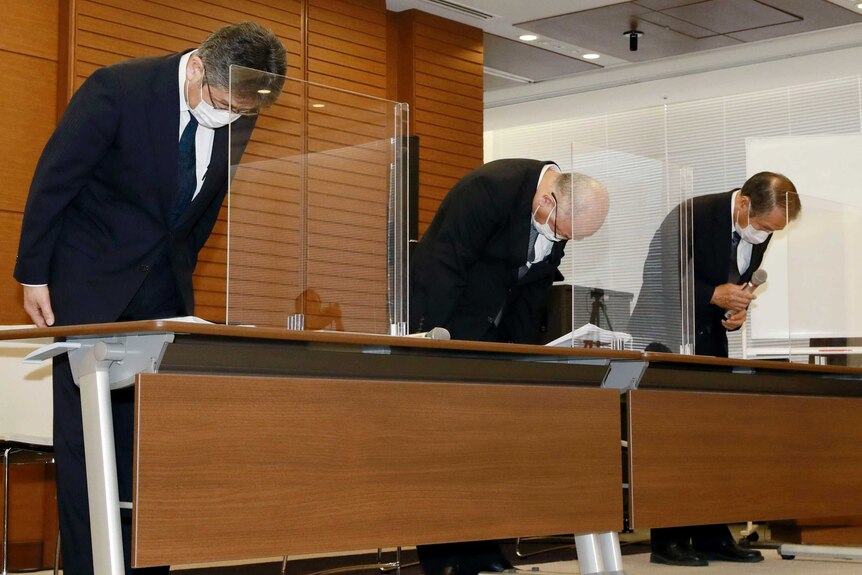 Three Japanese men bow over a desk.