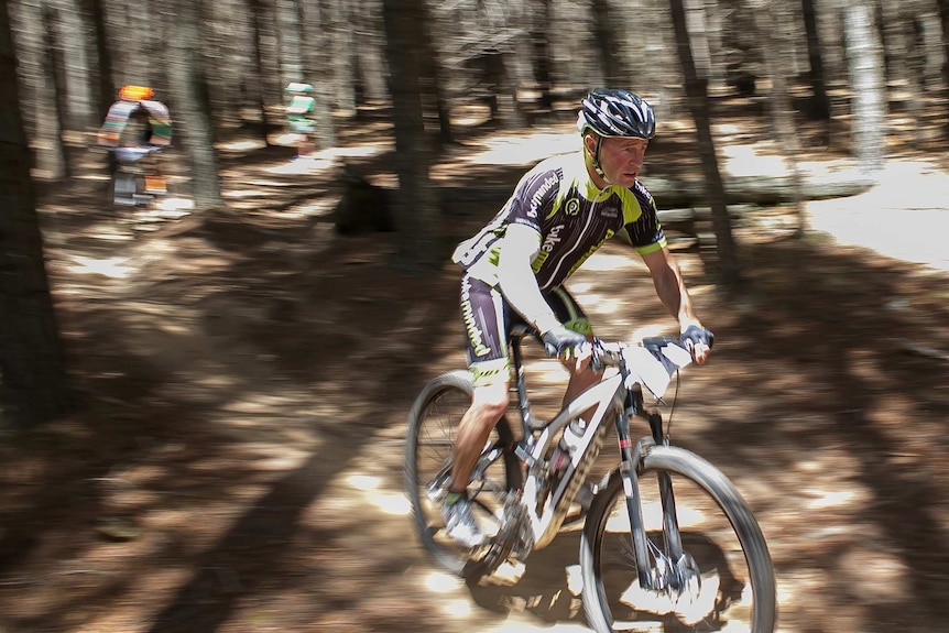 Action shot of a man riding a mountain bike through a blurred background of a forest