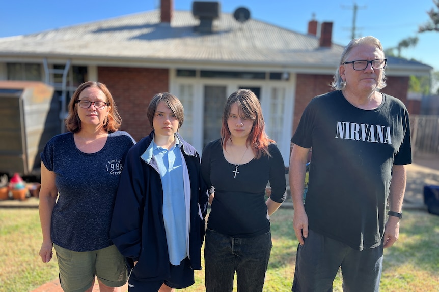 A family of four standing out the front of a single-story house