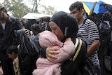 A migrant holds a child under the rain close to the border crossing between Greece and Macedonia
