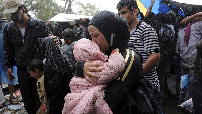 A migrant holds a child under the rain close to the border crossing between Greece and Macedonia