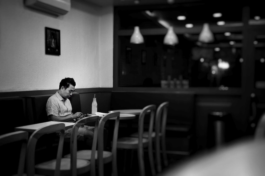 A man sits alone in a cafe. He's looking at his phone