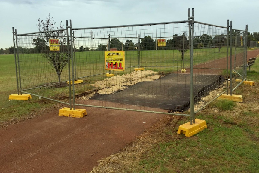 The bitumen bump sits behind a fence on a bike path in the park.