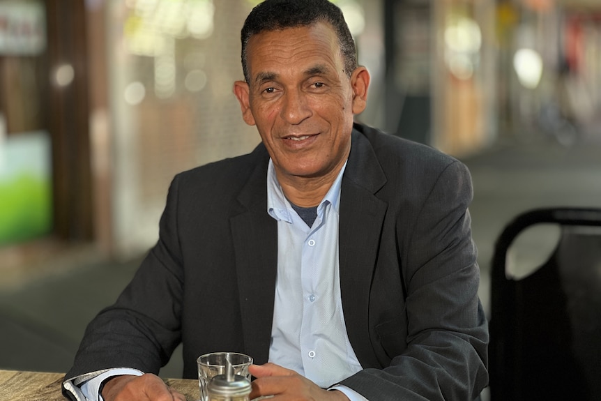 A man in a suit sitting at a cafe table.