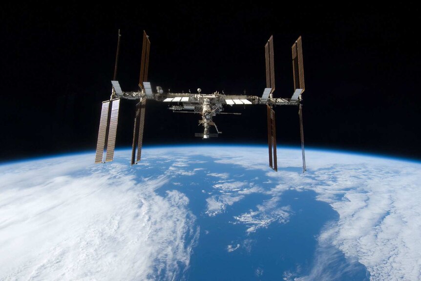 A space station above the Earth. The space station is shaped like a giant H.
