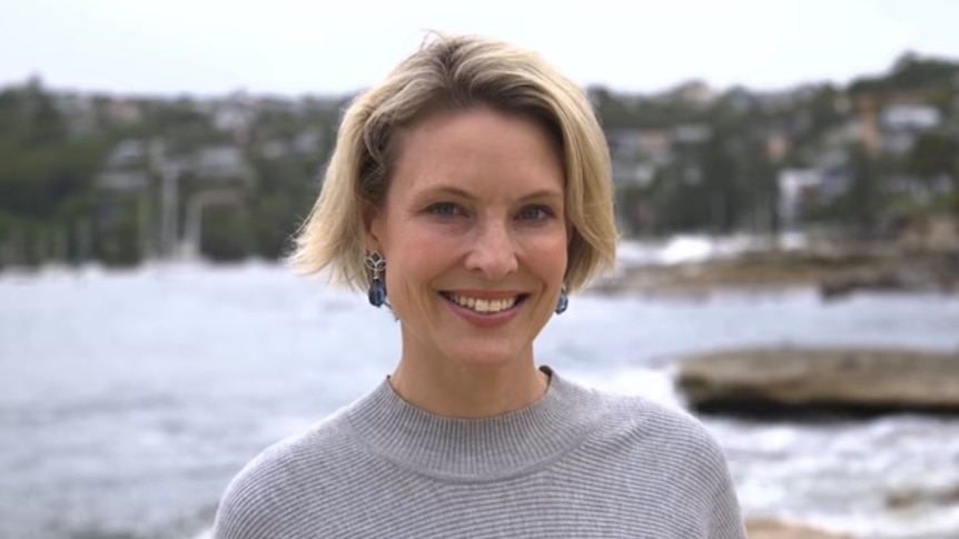 A blonde woman looks at the camera in a coastal setting