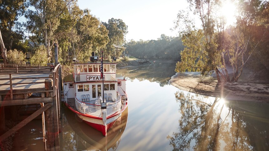 a paddle steamer at a jetty on a wide, tree-lined river.