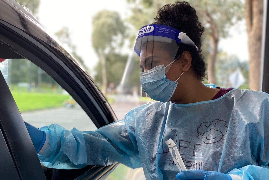 A health worker in full PPE offers a coronavirus test to the driver of a car.