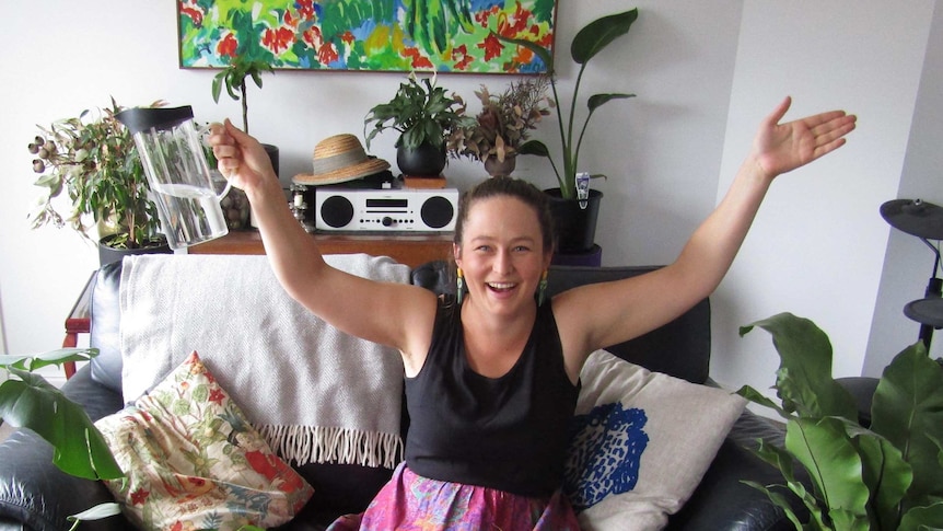 Hobart freelance writer Zoe Keans sitting on a couch surrounded by various lush indoor plants.