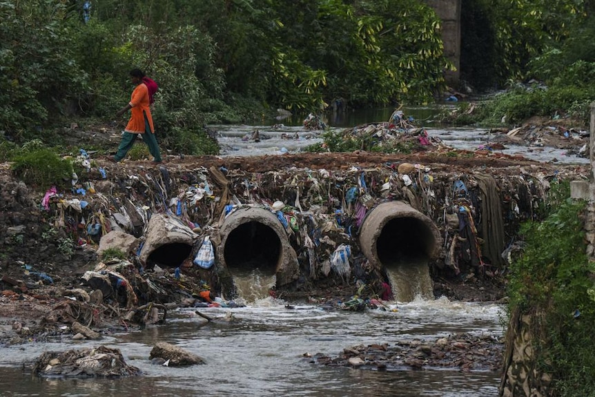 A woman walks over drainage pipes that flow into the Bagmati River in Kathmandu, littered with pollution 