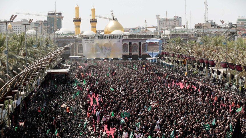 Hundreds of Shi'ite pilgrims gather in front of a shrine with a gold dome.