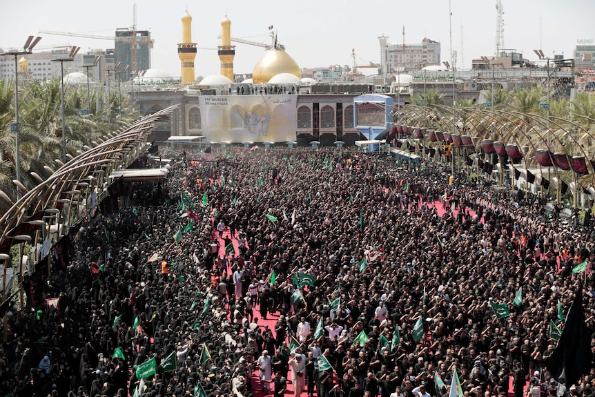 Hundreds of Shi'ite pilgrims gather in front of a shrine with a gold dome.