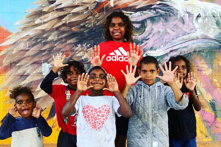Indigenous children standing in front of a wall mural.