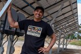 A man grinning and standing beneath a ground-mount solar array