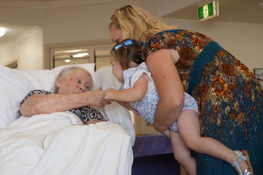 A woman holds her toddler daughter while she interacts with an aged care resident.