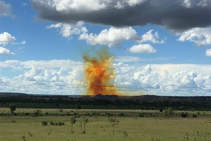 a noxious looking yellow plume of smoke rises in the distance surrounded by bushland