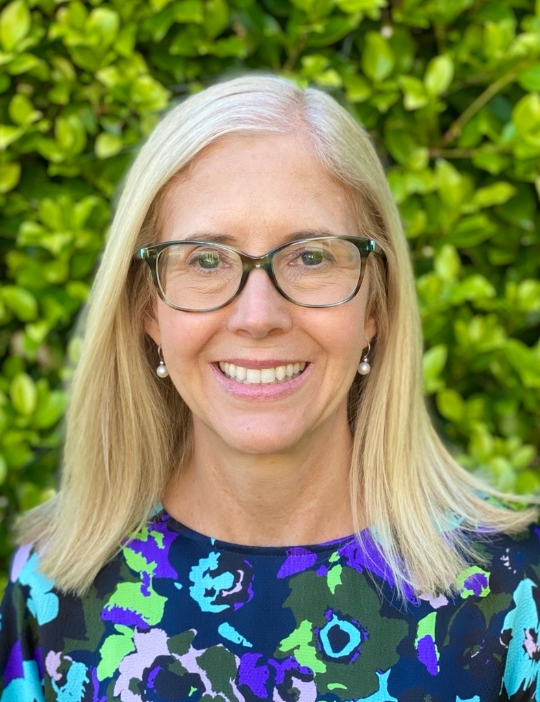 A white middle-aged woman with blonde, shoulder-length hair and glasses smiles at the camera
