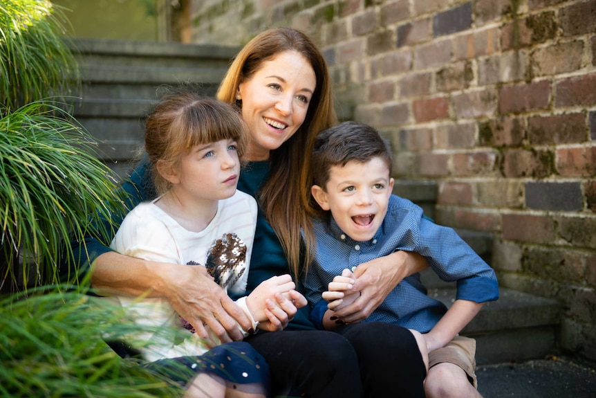 A smiling woman with dark hair sits on a step with two children.