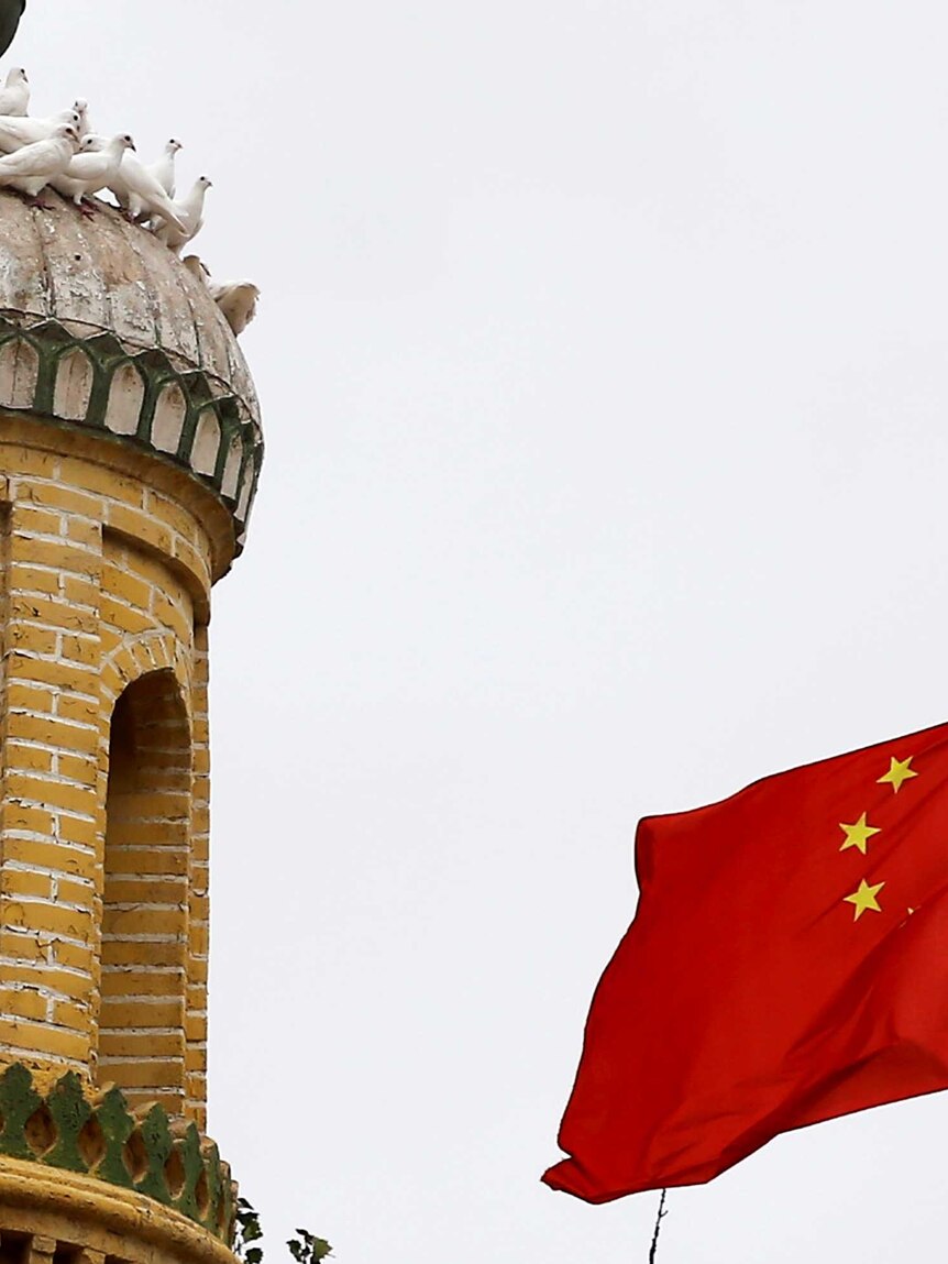 An old minaret with lots of white pigeons on it next to a fluttering Chinese flag, red with yellow stars.
