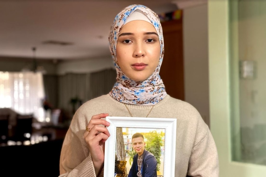 A woman in head scarf holds a picture of her husband.