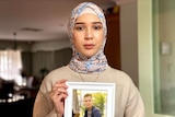 A woman in head scarf holds a picture of her husband.