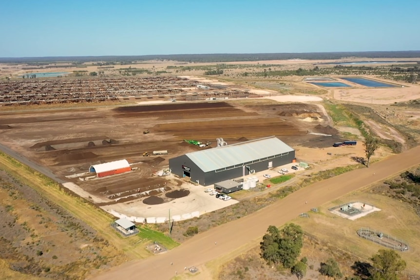 A high angle, aerial shot shows the factory and cattle surrounded by Australian red dirt.