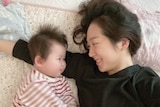 A mother and daughter lie down smiling at each other. 