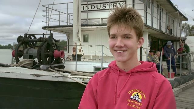 Boy stands in front of paddle steamer
