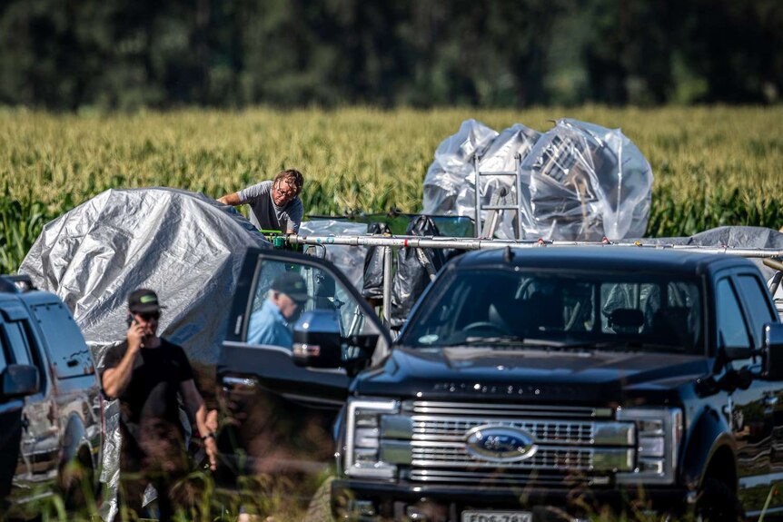 Vehicles and production crew are seen in a cornfield.