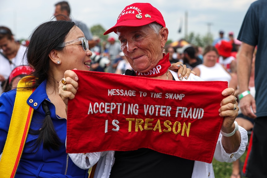 An elderly Trump supporter holds a sign that says 'Message to the swamp. Accepting voter fraud is treason'.