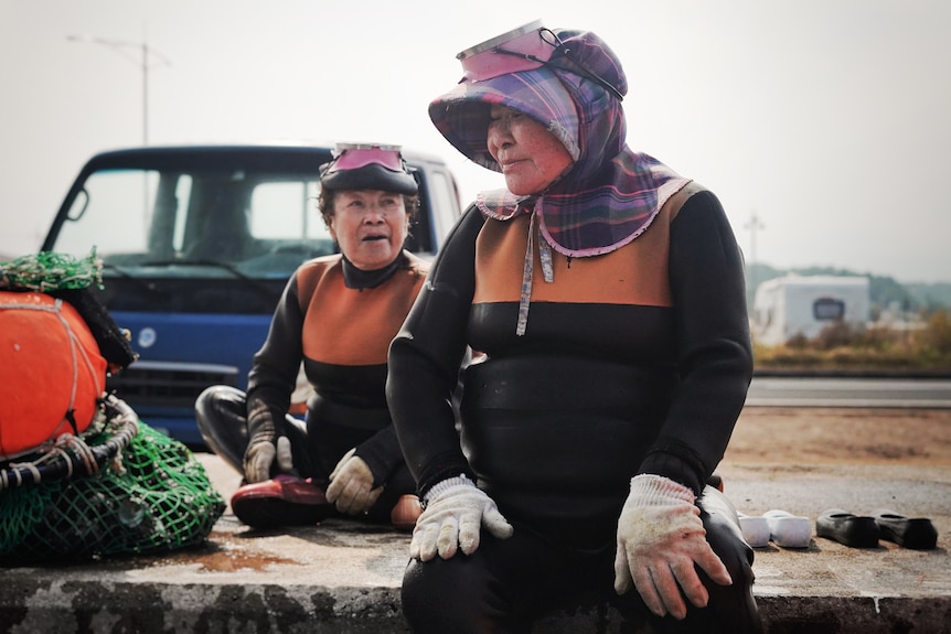 Two women talk and smile at each other dressed in full diving suits, hats and gloves.