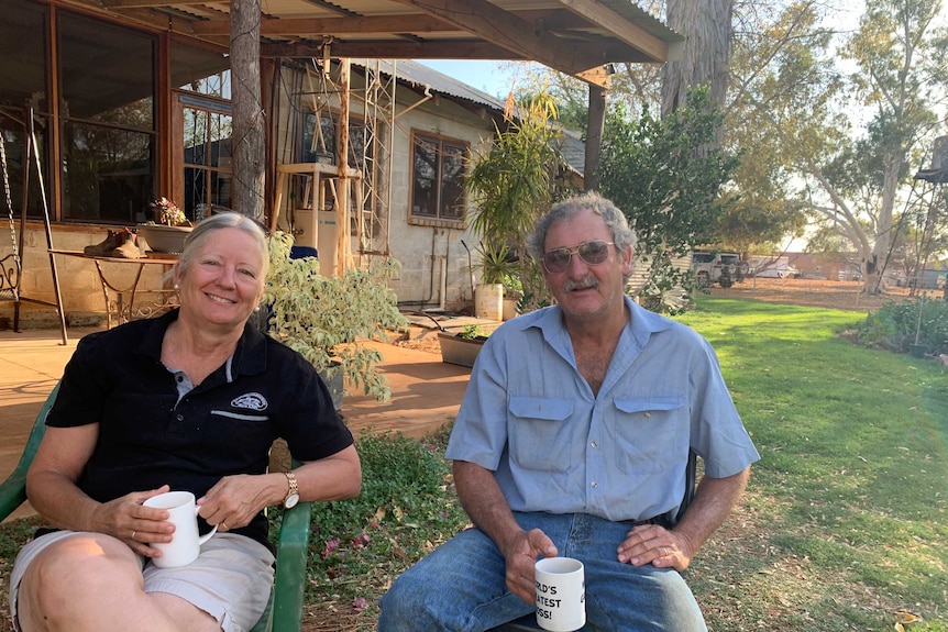 Two people sit on chairs outdoors holding mugs of tea