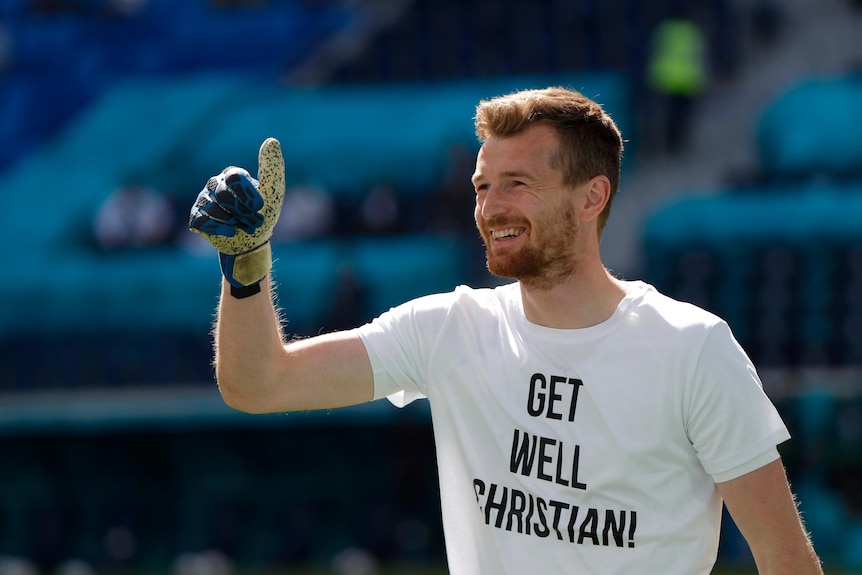 A Finnish goalkeeper wears a white T-shirt with the message 'Get well Christian!' warming up for a Euro 2020 game. 