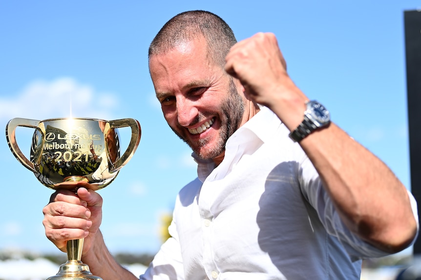A race horse owner holds the 2021 Melbourne Cup with his right hand.